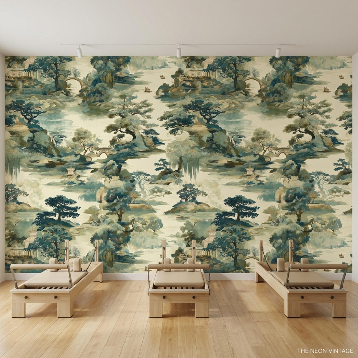 Three wooden Pilates reformers line a hardwood floor in front of a Chinoiserie landscape wallpaper accent wall.