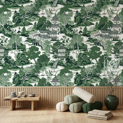 A wooden bench, stacked pillows, and a vase sit on a wooden floor against a green chinoiserie wallpaper wall.