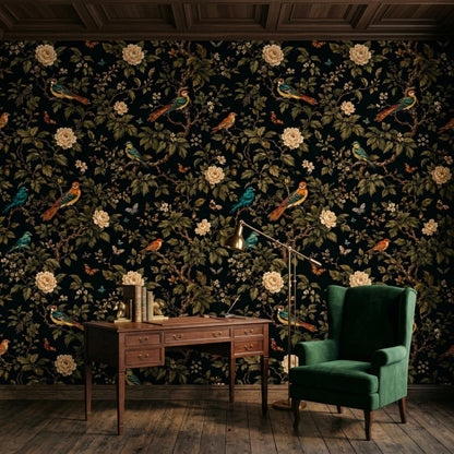 A dark wooden desk and a green velvet armchair are set against a dark floral wallpaper wall in a paneled room.