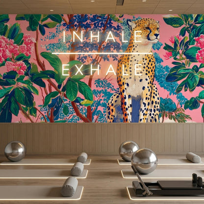 A gym setting features a row of exercise bikes in front of a pink leopard jungle wallpaper mural with glowing text.