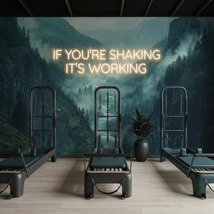Three Pilates reformers are arranged on a light wooden floor against a misty mountain valley mural and illuminated neon sign.