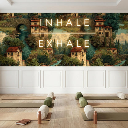 A yoga studio floor with rolled mats and bolster pillows is set against an Italian village wallpaper wall with glowing neon text.