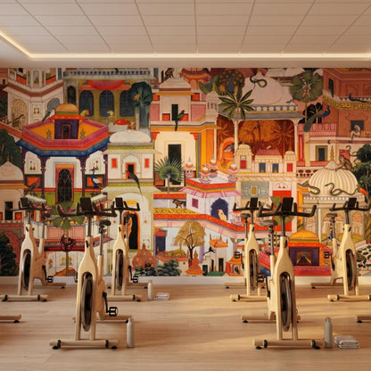 A gym interior with several exercise bikes lined up on a wooden floor in front of an expansive wall mural featuring Mughal-style palaces and jungle scenes.
