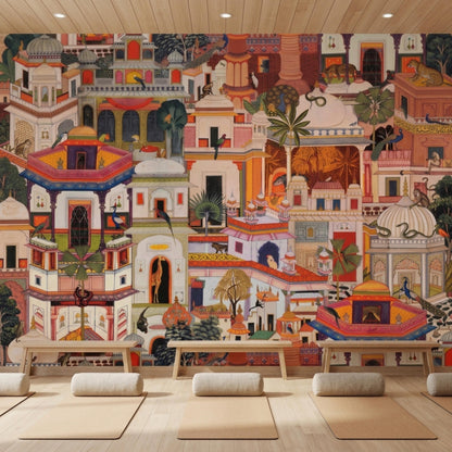 A yoga studio floor with rolled-out mats and bolster pillows, positioned in front of a colorful wall mural displaying traditional Indian palace architecture.