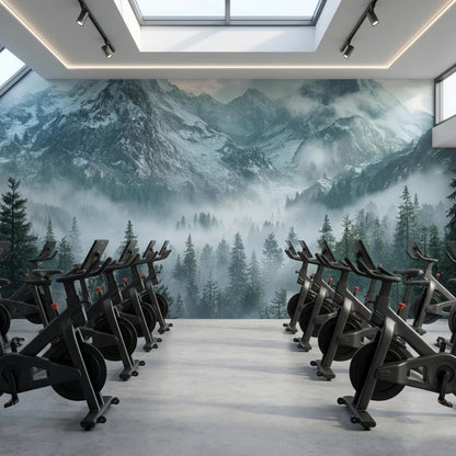 A row of exercise bikes faces a large misty mountain forest wall mural in a bright gym space.