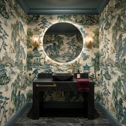 A bathroom with dark marble counters and a round mirror against a blue and green landscape wallpaper.