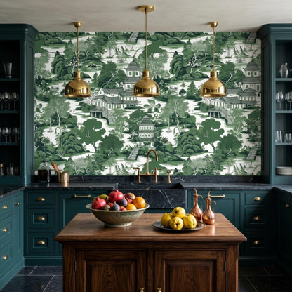 A kitchen features dark green cabinets, a wooden island, three brass pendant lights, and green chinoiserie wallpaper.