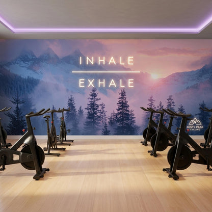 Indoor cycling studio with stationary bikes lined up against a misty mountain wall mural featuring illuminated neon text.