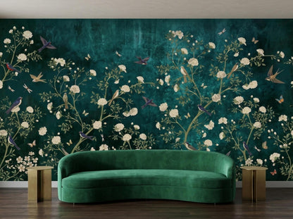 A modern curved green velvet sofa sits against a dark teal wall covered in an emerald botanical mural featuring white flowers and birds.