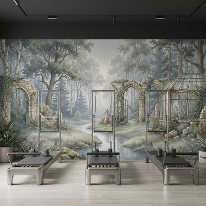 Three pilates reformer machines are lined up against a full-wall mural of a misty forest with stone arches.