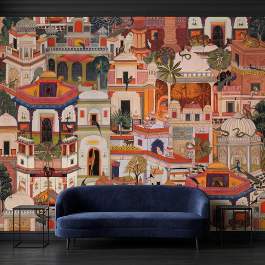 A vibrant Indian miniature-style wall mural depicting a palace complex with exotic animals, featuring a dark blue velvet sofa and two black side tables against a dark wall.