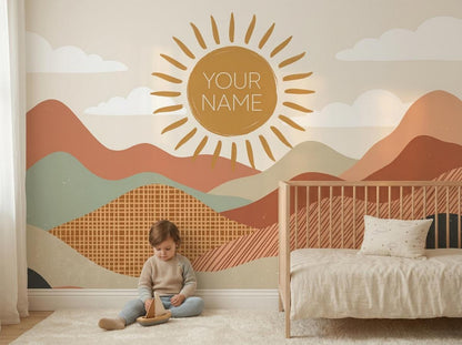 A child sits on a white rug playing with a wooden toy in front of a colorful boho sun and mountain wall mural featuring the text YOUR NAME.