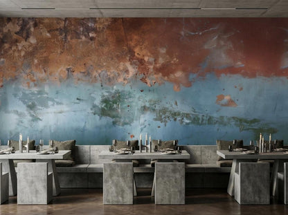 A dining space with concrete tables and benches set against a textured abstract wall mural in shades of copper and blue.