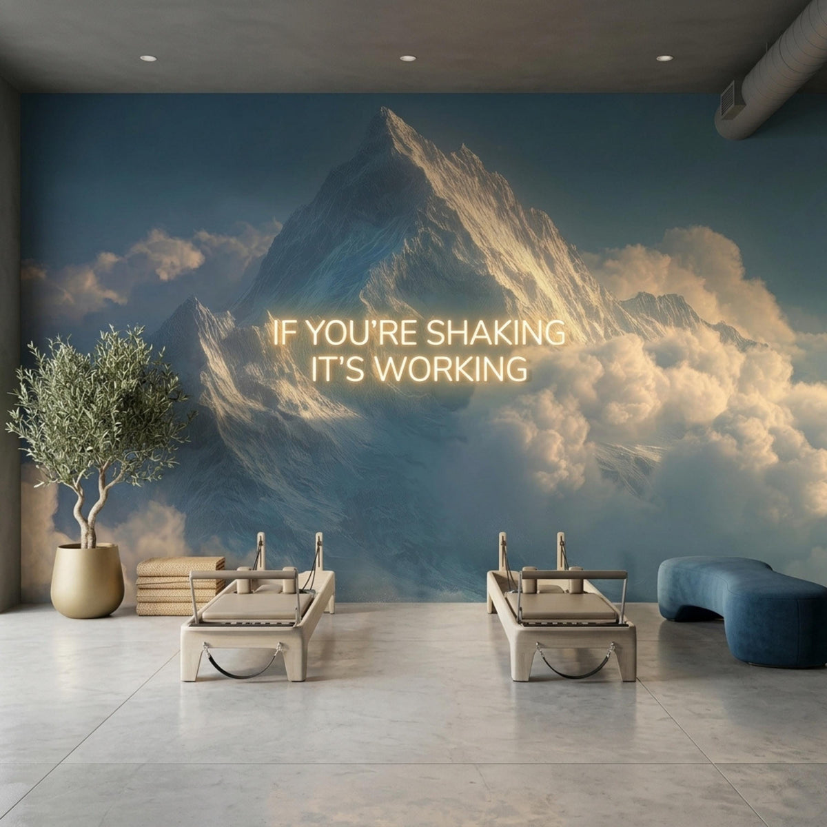 A wellness room with pilates reformers and a neon sign reading If You Are Shaking Its Working on a mountain mural.