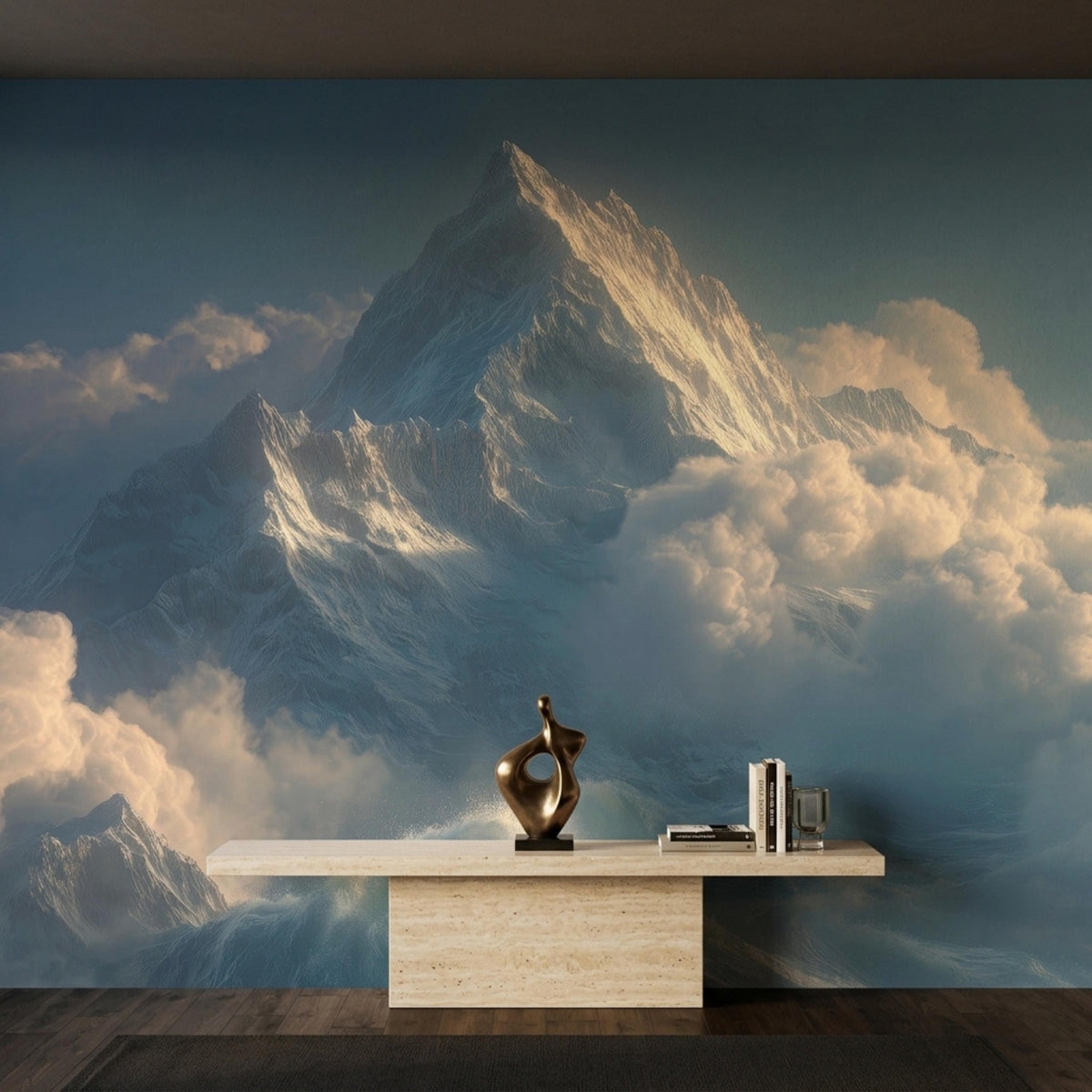 A long beige console table with books and a dark abstract sculpture sits against a mountain and cloud wall mural.