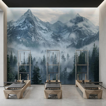 Three pilates reformer machines are arranged in a room with a panoramic misty mountain forest wall mural.
