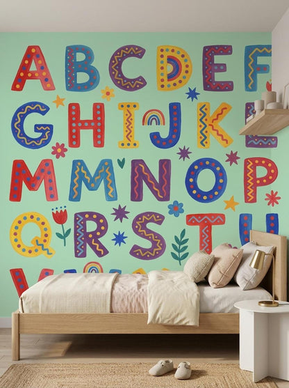 A child's bed with neutral bedding is placed against a mint green wall covered in colorful folk art alphabet letters.