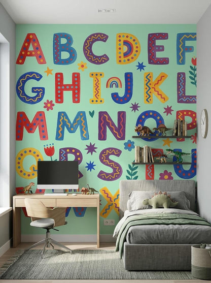 A boy's bedroom featuring a gray upholstered bed and a wooden desk set against a mint green wall with a folk art alphabet mural.