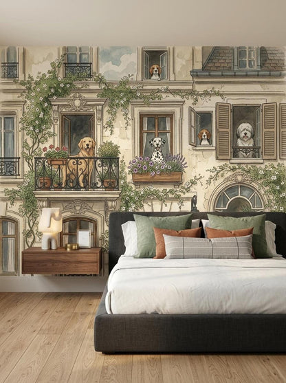 A watercolor wallpaper mural featuring a European city building with illustrated dogs in windows, displayed behind a bed with dark grey upholstery and green pillows.