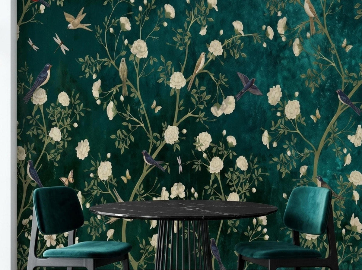 A black dining table and green velvet chairs are set against a dark teal chinoiserie wallpaper mural.