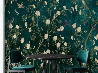 A black dining table and green velvet chairs are set against a dark teal chinoiserie wallpaper mural.