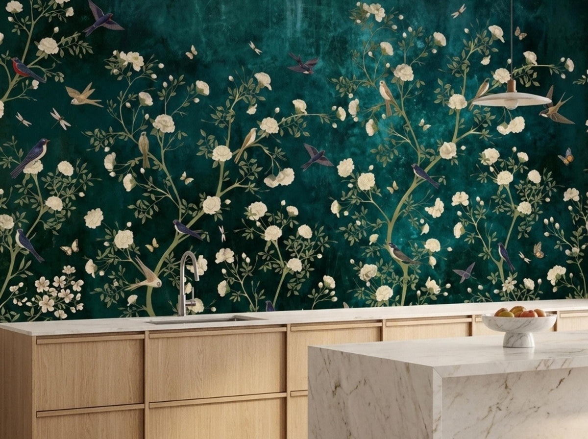 A kitchen counter and marble island sit in front of a moody teal botanical wallpaper mural with white blossoms and birds.