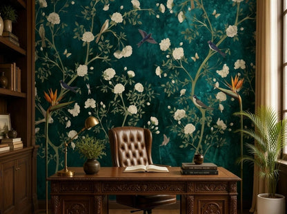 A brown leather desk and potted plant are placed in a home office with an emerald floral and bird wallpaper mural.