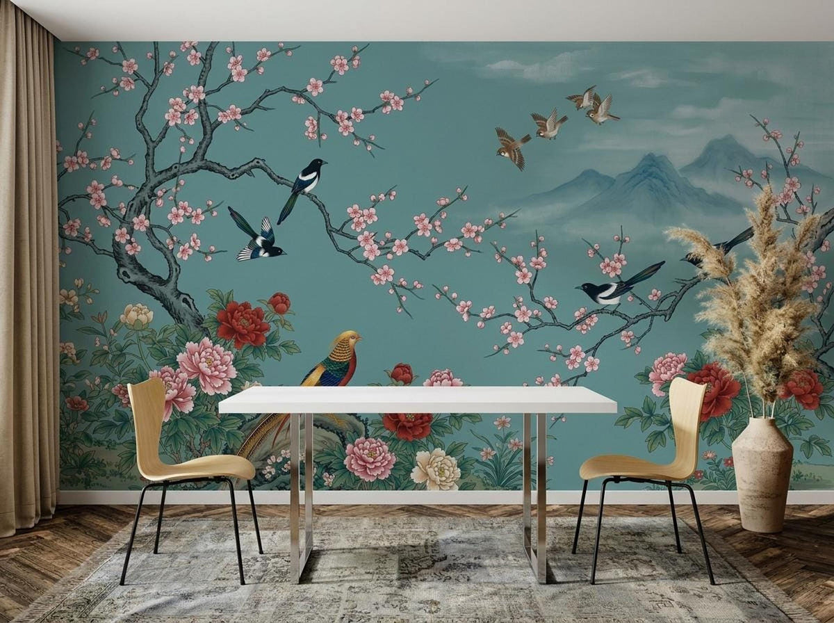 A teal floral and bird wall mural serves as the backdrop for a dining area with a white table, two yellow chairs, and a tall vase of dried pampas grass.