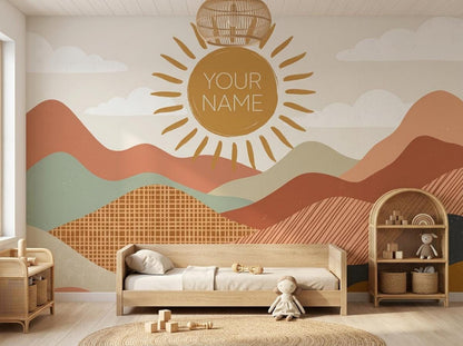 A childs room features a large boho sun and mountain wall mural with YOUR NAME, flanked by two low wooden shelving units and a wooden daybed.
