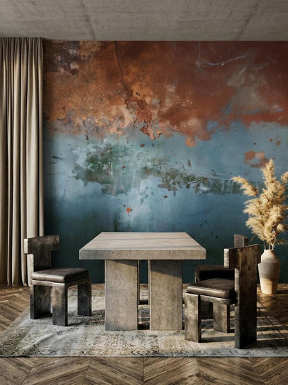 A dining table and chairs on a patterned rug against an abstract weathered copper and blue wall mural.