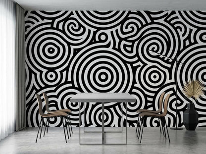 A dining space with a rectangular table and chairs positioned against a wall covered in black and white concentric circle wallpaper.