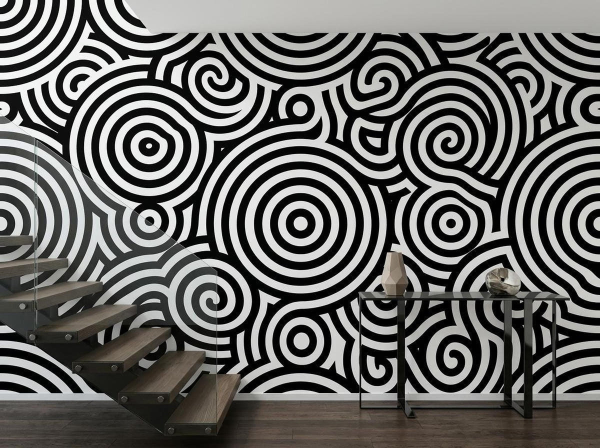 A staircase next to a wall covered in black and white abstract geometric wallpaper and a slim console table.