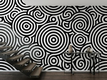 A staircase next to a wall covered in black and white abstract geometric wallpaper and a slim console table.
