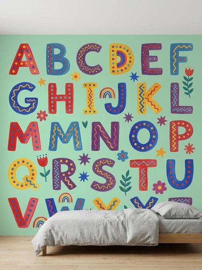 A gray bed is neatly made against a mint green accent wall displaying a colorful folk art alphabet pattern.