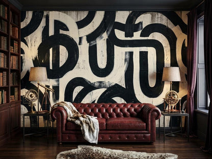 A room featuring a large black and white abstract brushstroke wallpaper, a red leather tufted sofa, and a built-in bookcase.