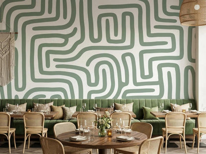 A dining space with a sage green maze mural on the back wall above a green cushioned banquette seating and wooden tables.