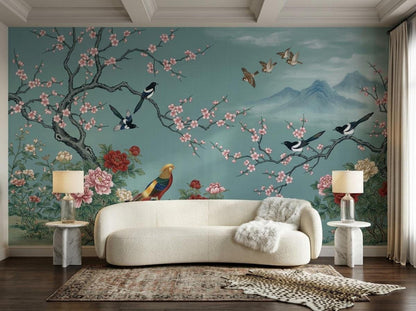 A teal chinoiserie accent wall with blossom branches and birds is framed by a white sofa, two marble side tables with lamps, and an animal print rug.
