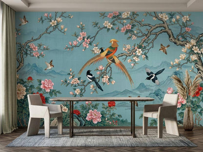 A dining table with two light gray chairs placed in front of the teal floral and bird wallpaper mural.