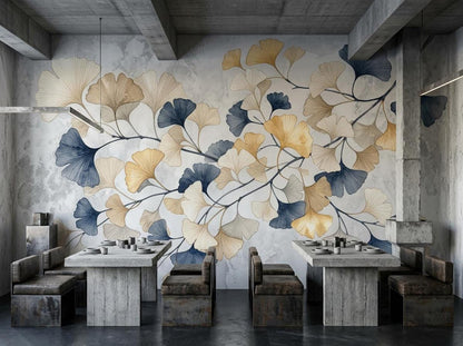 A restaurant or dining area with concrete tables and dark chairs set against a striking wall mural of branching ginkgo leaves in gold, beige, and deep blue.