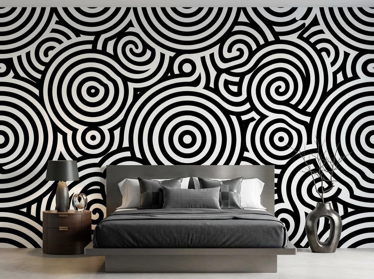 A bedroom with a bed featuring gray linens against a wall with a large scale black and white concentric circle mural.