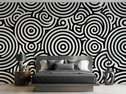 A bedroom with a bed featuring gray linens against a wall with a large scale black and white concentric circle mural.