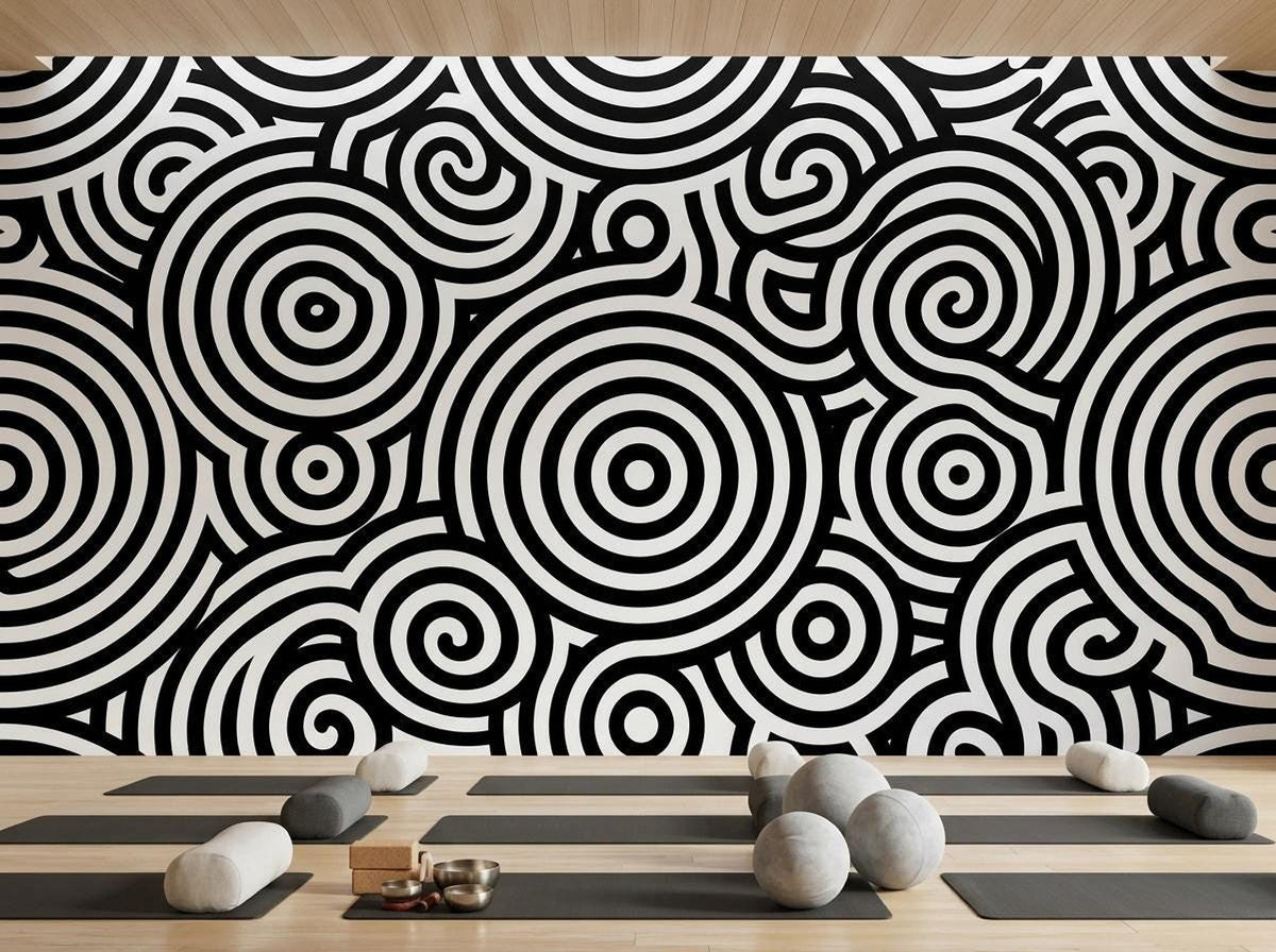 A yoga studio floor with mats, bolsters, and meditation cushions placed in front of a black and white abstract wallpaper mural.