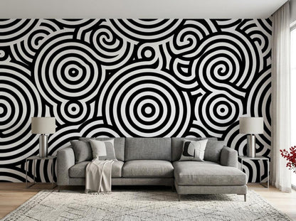 A living room features a black and white geometric patterned accent wall behind a gray sectional sofa and a patterned rug.