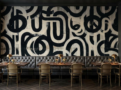 A restaurant dining room with gray tufted booth seating, wooden tables, and gold-framed chairs in front of an abstract black and white brushstroke mural.