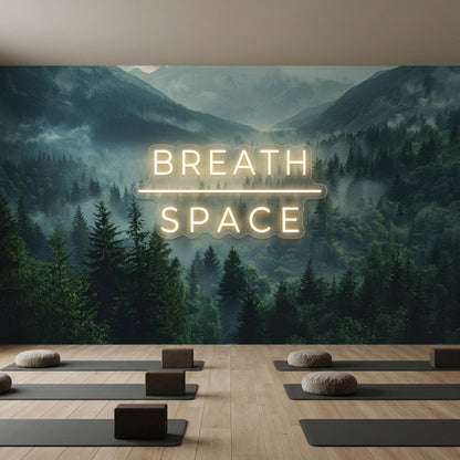 A yoga studio floor has several mats and cushions arranged in front of a wall mural showing misty mountains and a glowing neon sign.