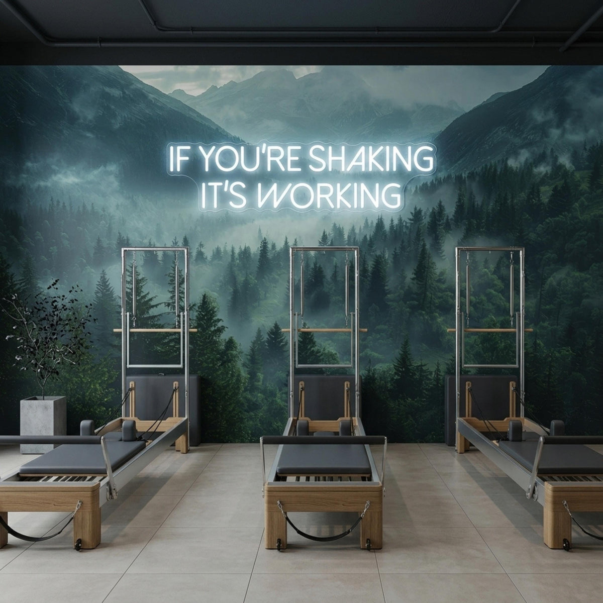 A pilates studio displays three reformer machines positioned against a dark wall mural of a foggy pine forest with a glowing neon quote.