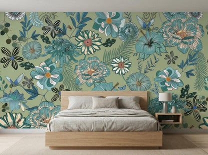 A wooden bed with grey bedding is placed in front of a sage green botanical wallpaper mural featuring large blue flowers and hummingbirds.