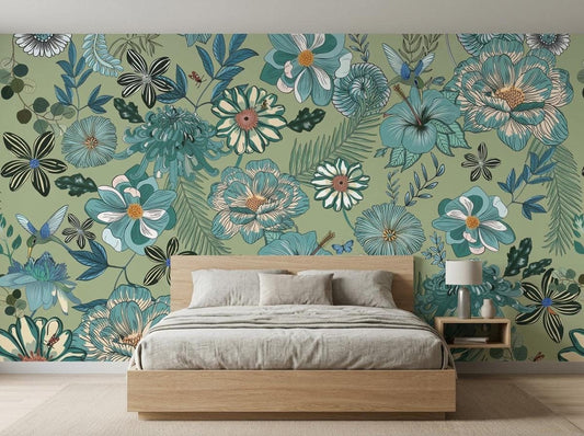 A wooden bed with grey bedding is placed in front of a sage green botanical wallpaper mural featuring large blue flowers and hummingbirds.