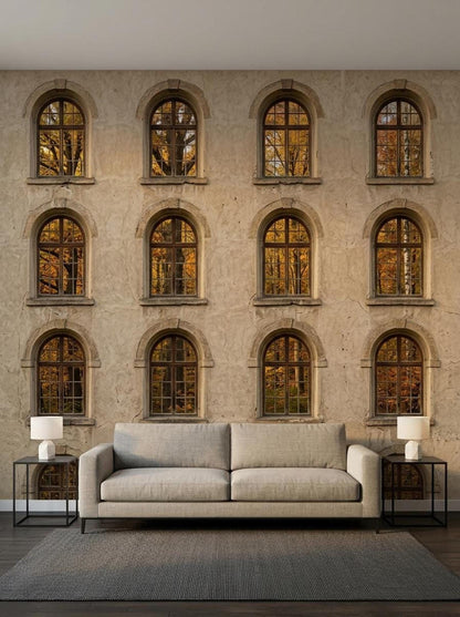 A minimalist living room setting with a light gray sofa and two matching side tables positioned in front of an architectural stone facade wallpaper mural with autumn forest window views.