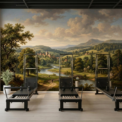 A gym or physical therapy room with three black pilates reformers positioned in front of a large vintage landscape wall mural.